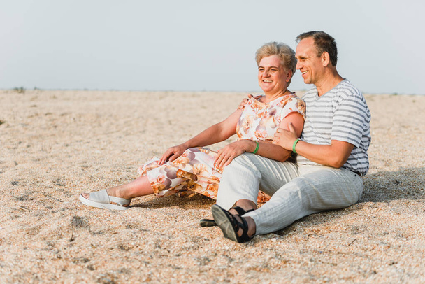 Romantic adult couple standing together on the beach. Mature pair relax at the seaside on holiday. Happy familiy walking and holding hands near sea. Husband embracing wife. Love story near the sea - Foto, afbeelding