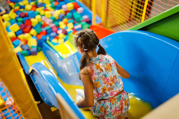 Meisje rijdt op plastic kinderglijbaan, speeltuin in amusementscentrum. Speeltuin binnen, speelkamer - Foto, afbeelding