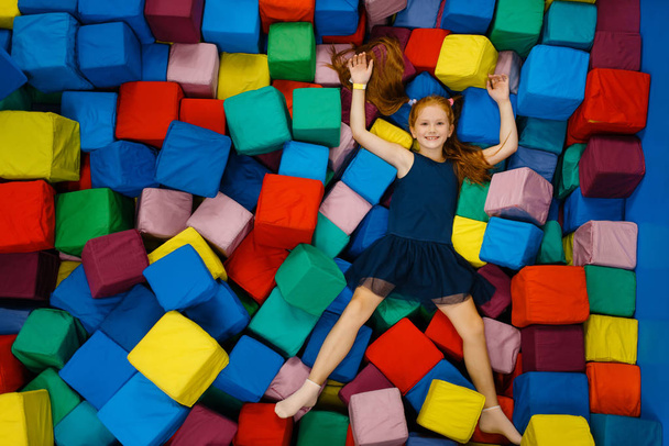 Petite fille mignonne couchée en cubes doux, aire de jeux dans le centre de divertissement. Aire de jeux intérieure, salle de jeux
 - Photo, image