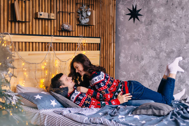 pareja enamorada en hermosos suéteres yacen en la cama. acogedora habitación y C - Foto, Imagen