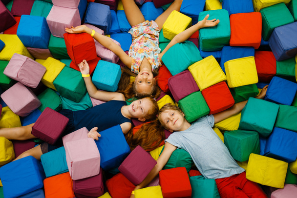 Niños felices acostados en cubos suaves, parque infantil en el centro de entretenimiento. Zona de juegos interior, sala de juegos
 - Foto, imagen