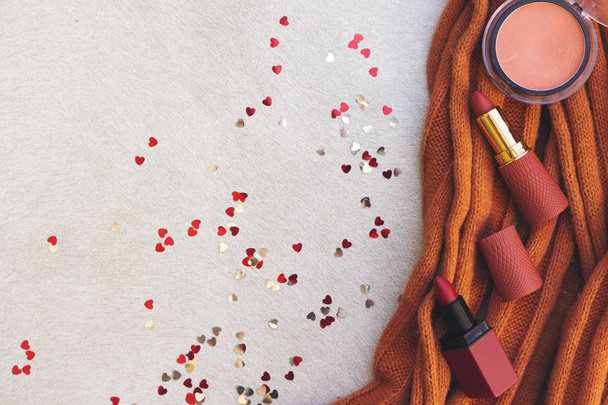 lipstick and pink blush on woolen orange scarf decorated with heart confetti  - Foto, Bild