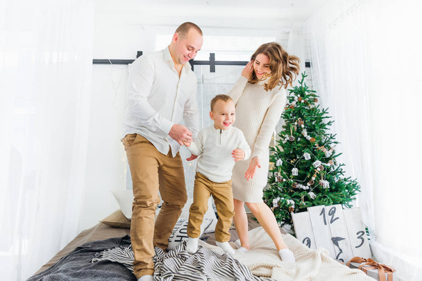 子供と親が手を取り合ってベッドに飛び込む。クリスマス  - 写真・画像