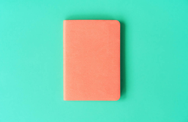 Libro naranja con cubierta de cuero artificial sobre fondo de menta. Concepto de documento minimalista en colores de moda. Regreso a la idea escolar
 - Foto, imagen