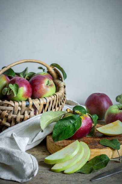 Juicy ripe apples in a wicker basket and kitchen utensils on a wooden table on a light wall background in Scandinavian style, concept of organic food, harvest, gardening - Fotoğraf, Görsel