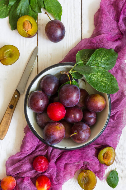 Juicy plums and purple runner on a white wooden background pattern with copy space for text flat top view - Fotoğraf, Görsel