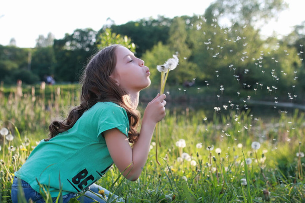 Подросток выдувает семена из цветка одуванчика в весеннем парке
 - Фото, изображение