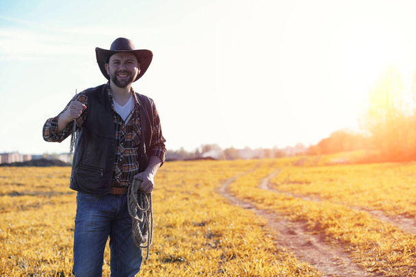 A man cowboy hat and a loso in the field. American farmer in a f - Photo, Image