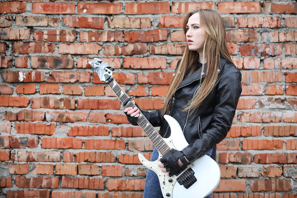  Een rock muzikant meisje in een leren jas met een gitaar  - Foto, afbeelding