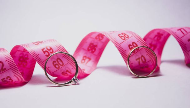 A pink centimeter tape and a wedding ring near it. The concept of wedding, diet. There is a place for text. - Photo, Image