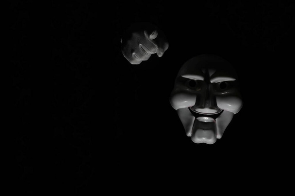 Máscara assustadora branca em um fundo preto com mão branca
. - Foto, Imagem