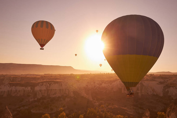 sunrise photo in Cappadocia with big air balloons in the sky over sandy hills - Photo, Image