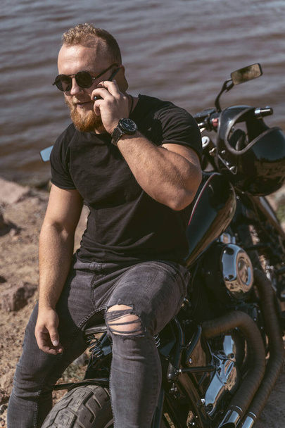 Confident bearded man lying on bike talking on the phone - 写真・画像