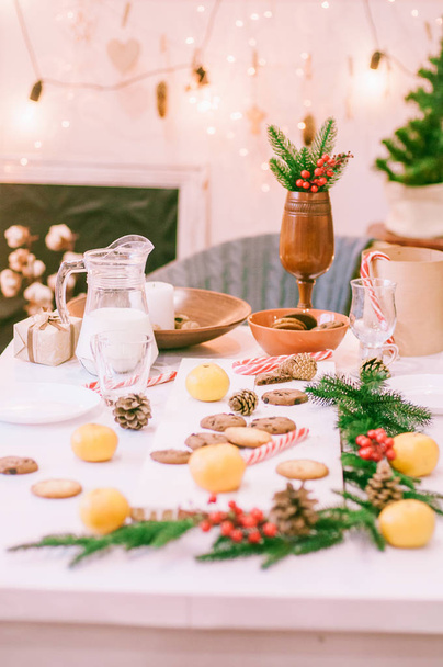 Room and table decorated for Christmas. Christmas table in gingerbread cookies, milk, tangerines and needles. Christmas mood - Φωτογραφία, εικόνα