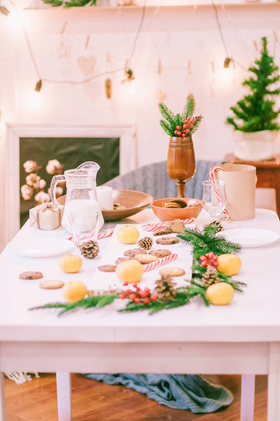Room and table decorated for Christmas. Christmas table in gingerbread cookies, milk, tangerines and needles. Christmas mood - Фото, изображение