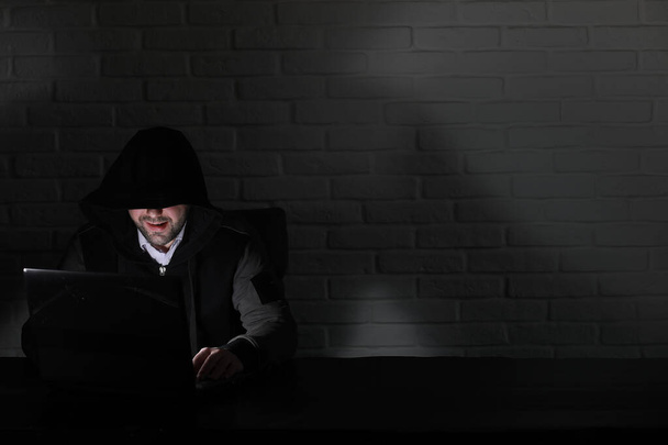 Hacker en masque noir et capuche à la table
 - Photo, image