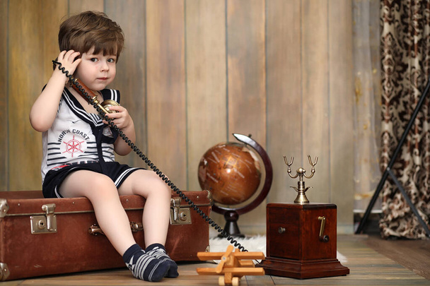 Ένα παιδί σε ένα ρετρό εσωτερικό και ένα παλιό τηλέφωνο κάθεται στο πάτωμα.  - Φωτογραφία, εικόνα