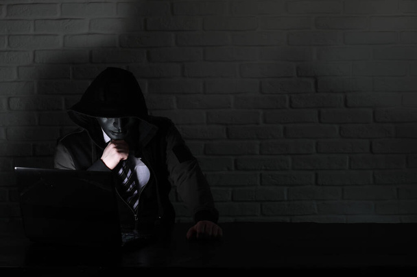 Хакер в чорній масці і капюшоні за столом
 - Фото, зображення