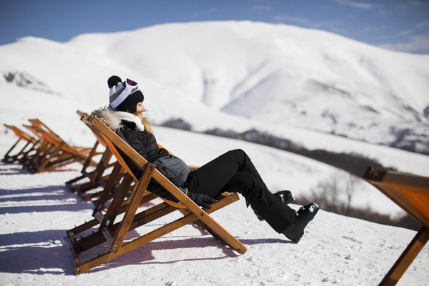 Νεαρή γυναίκα σκιέρ χαλαρώνοντας σε μια καρέκλα lounge μετά το σκι στα βουνά το χειμώνα - Φωτογραφία, εικόνα