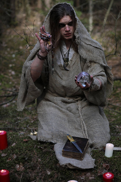 Un hombre en una sotana pasa un ritual en un bosque oscuro
 - Foto, imagen