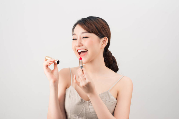 Photo of a beautiful young pretty asian woman with healthy skin posing naked isolated over white wall background holding lipstick. - Photo, Image