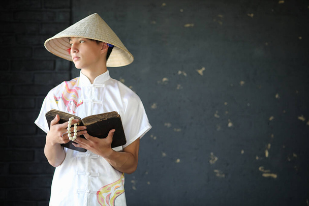 Aziatische jonge monnik in de hoed op zwarte muur - Foto, afbeelding