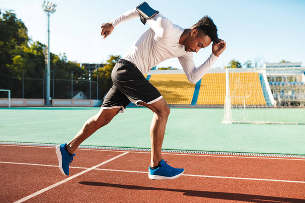 Vue latérale du jeune sportif afro-américain attrayant qui court sur l'hippodrome au stade de la ville
 - Photo, image