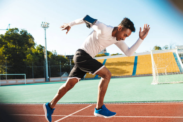 Вид сбоку на молодого афроамериканского спортсмена, бегущего по ипподрому во время тренировки на городском стадионе
 - Фото, изображение