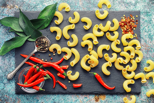 Uncooked pasta on a stone background. With seasonings and spices - Photo, Image