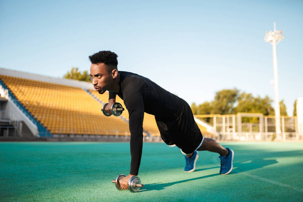 Giovane forte serio sportivo afroamericano che fa esercizi con manubri allo stadio
 - Foto, immagini