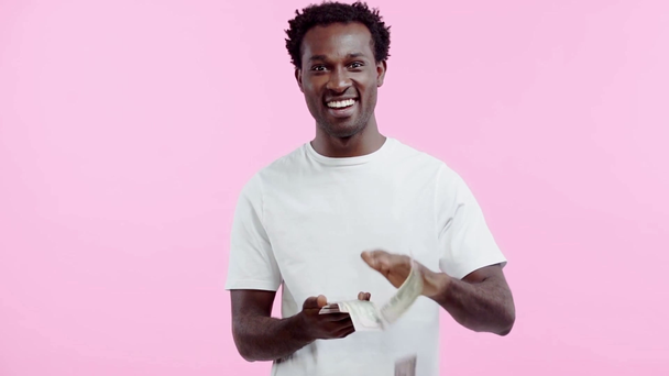 Zeitlupe eines afrikanisch-amerikanischen Mannes, der Dollars isoliert auf rosa hält - Filmmaterial, Video