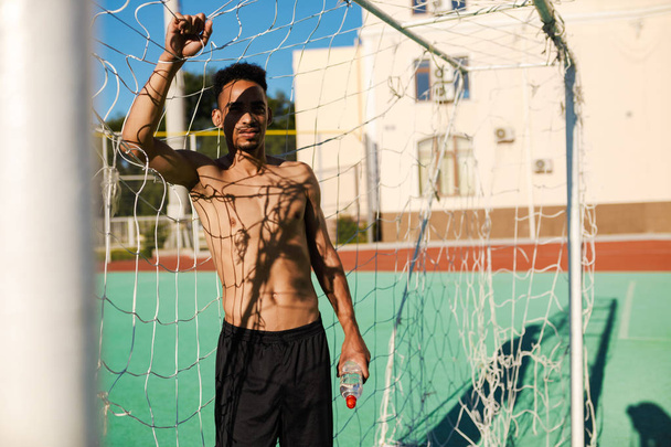 Fiatal vonzó félmeztelen afro-amerikai sportoló áll futball cél után játék a városi stadionban - Fotó, kép