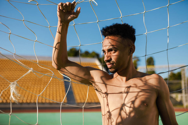 Retrato de un atractivo deportista afroamericano sin camisa mirando cuidadosamente hacia otro lado en el gol de fútbol en el estadio de la ciudad
 - Foto, imagen