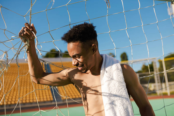 Portrait de sportif afro-américain torse nu avec serviette sur l'épaule dans le but de football après le match au stade de la ville
 - Photo, image