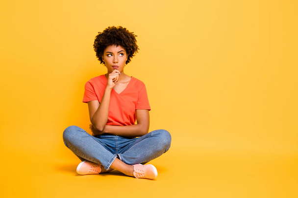 Full length body size photo of pensive solving deciding minded girlfriend sitting with her legs crossed wearing jeans denim t-shirt touching her chin isolated over yellow vivid color background - Fotó, kép