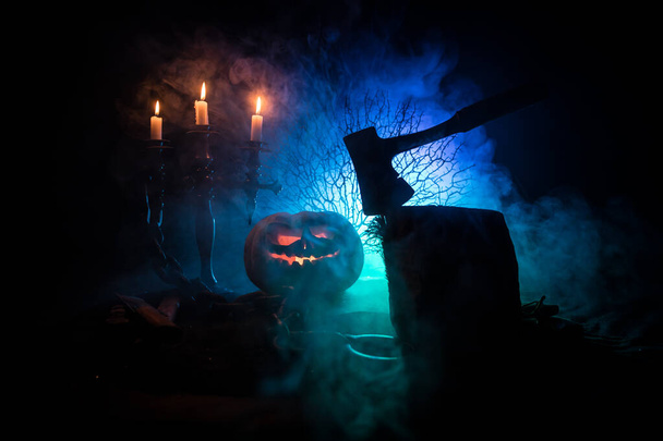 Scary orange pumpkin with carved eyes and a smile with burning candles and an ax - Photo, Image