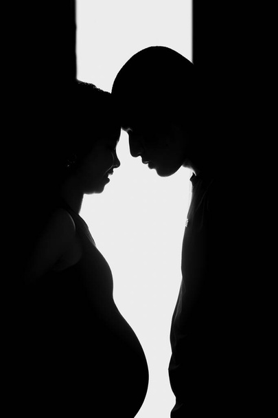 Vertical silhouette shot of a pregnant woman and a man with their foreheads against each other - Fotografie, Obrázek