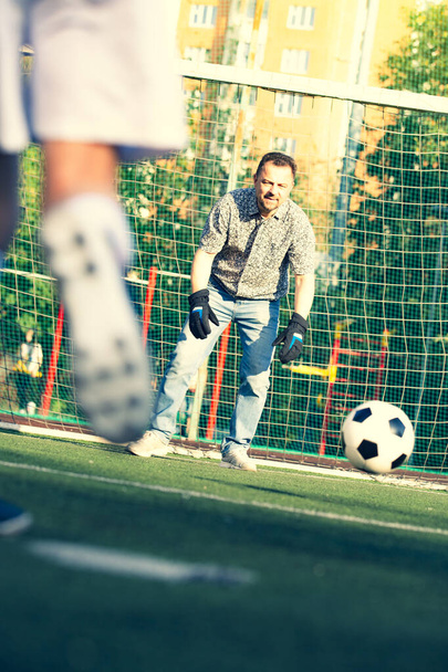 Father training his little son play in football. Man with child playing football outside on field. Kid approach dad in goal during family football game - 写真・画像