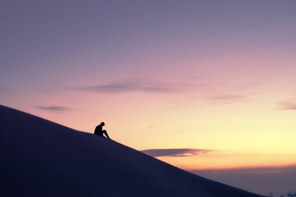 Žena uvažující o obzoru v poušti z vrcholu duny rýsující se proti zlaté obloze při západu slunce. - Fotografie, Obrázek