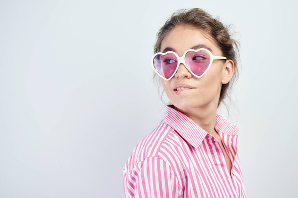 Brunette girl in pink clothes and glasses with envy and regret bites her lip and looks at copy space - Foto, imagen