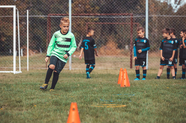 Jonge speler in voetbal trui loopt tussen kegels en ring jongen - Foto, afbeelding