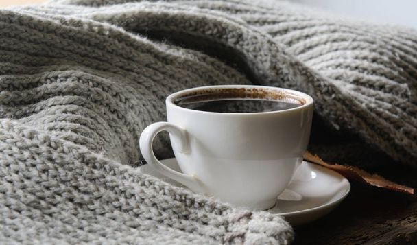 Winterochtend. Op een vintage board ligt een trui. In een trui een stomende kop koffie. Concept - 's morgens koffie, warm houden - Foto, afbeelding