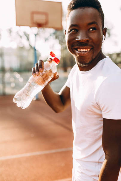Young athletic African-American, at a sports stadium, holding a bottle of water - Foto, immagini