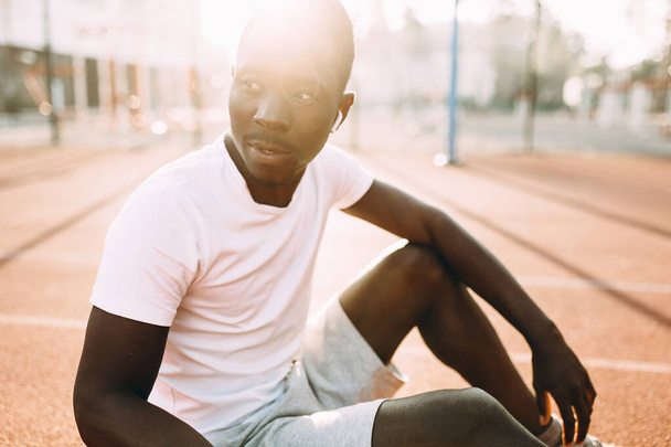 Sporty African American posing sitting on court at dawn, morning exercise - Φωτογραφία, εικόνα