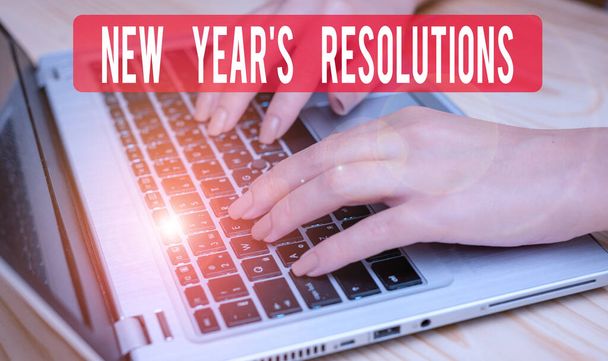 Text sign showing New Year S Resolutions. Conceptual photo Wishlist List of things to accomplish or improve woman laptop computer smartphone mug office supplies technological devices. - Photo, Image