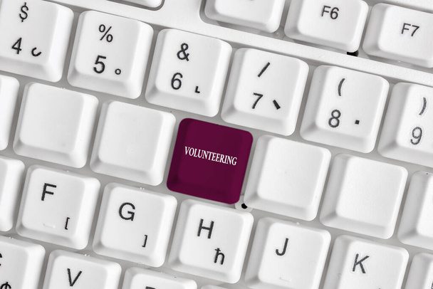 Text sign showing Volunteering. Conceptual photo Provide services for no financial gain Willingly Oblige White pc keyboard with empty note paper above white background key copy space. - Fotoğraf, Görsel