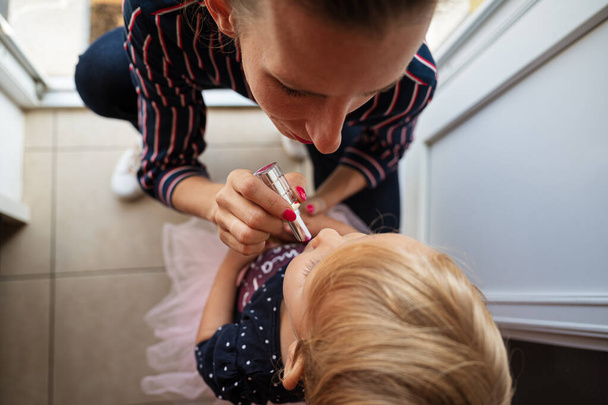 La madre joven a la moda se arrodilla para aplicar el lápiz labial rosado en
 - Foto, Imagen
