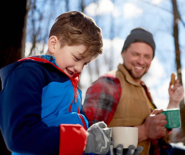 Family with son enjoying playing in fresh snow during wintertime and having hot chocolate during a picnic - Foto, Imagem