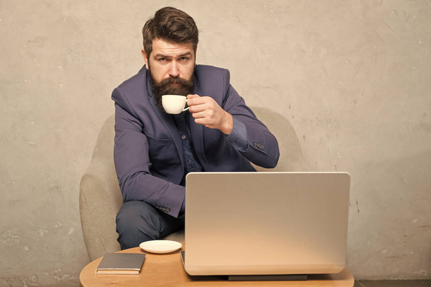 In mobile style. Bearded man enjoying his hot drink and mobile internet. Businessman with mobile device drinking tea or coffee at workplace. Hipster in formalwear working at laptop in mobile office - Fotografie, Obrázek