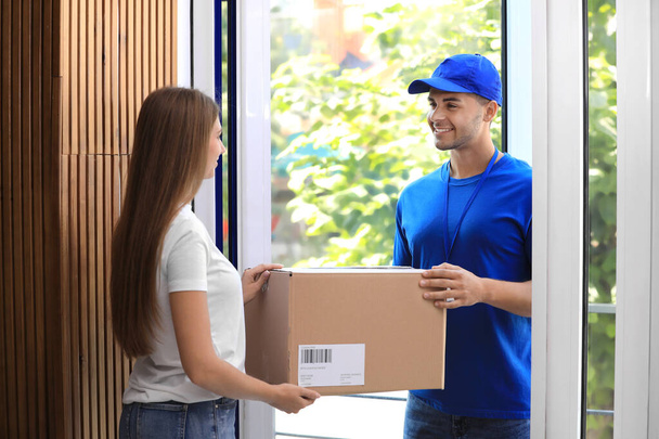 Woman receiving parcel from courier on doorstep - 写真・画像